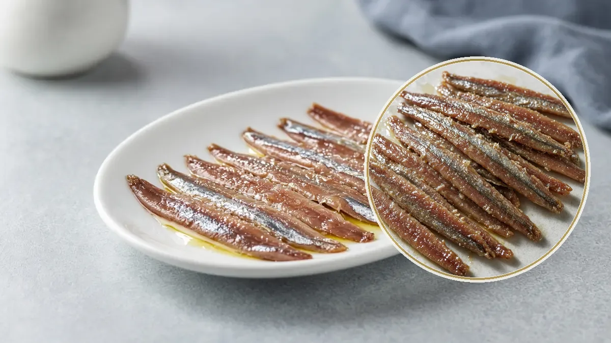Filetes de anchoa plateados y brillantes, alineados en un plato ovalado blanco.
