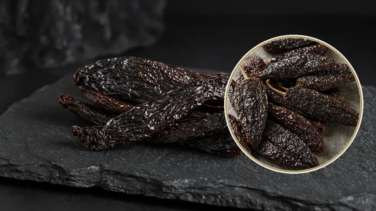 Chiles pasilla largos, delgados y casi negros se amontonan sobre una tabla de pizarra oscura.