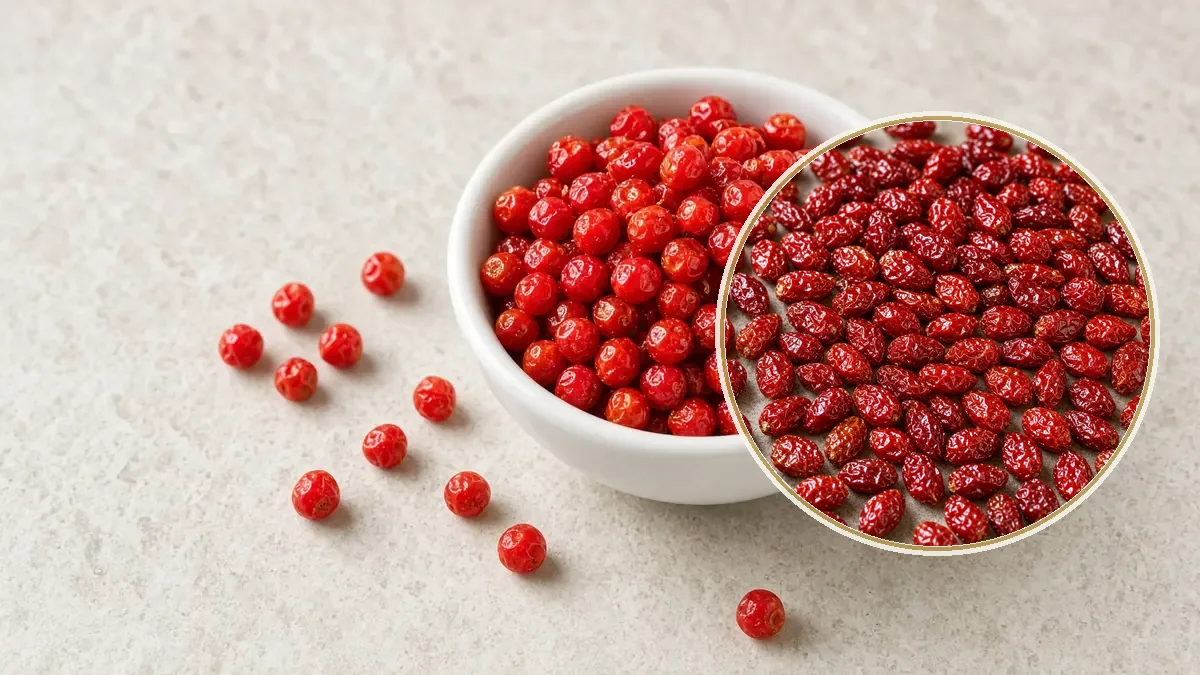 Un ramekin blanco guarda un montoncito de chiles piquín muy pequeños y rojos, sobre piedra caliza clara.